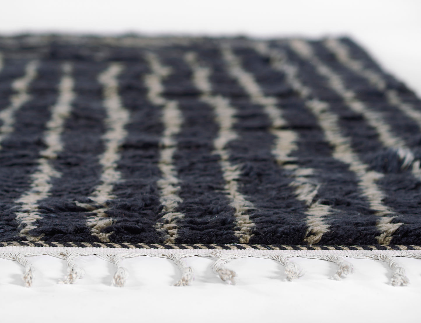 Close-up of navy shag rug with cream vertical stripes and fringed edge.