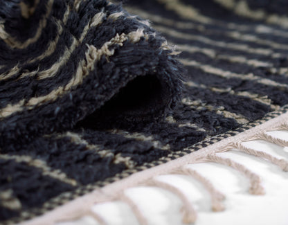 Close-up of a navy rug with cream geometric stripes, thick plush pile, rolled edge and beige tassel fringe.