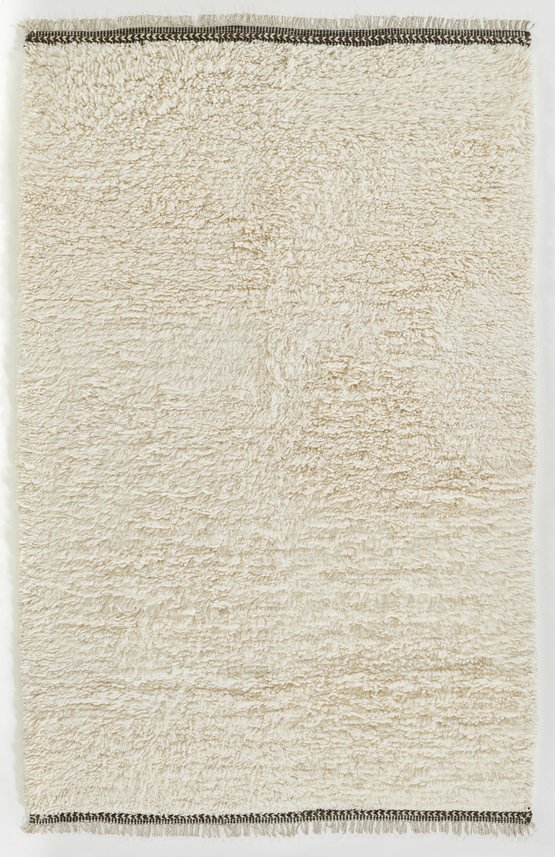 Rectangular cream shag rug with plush pile and dark braided borders along the ends.