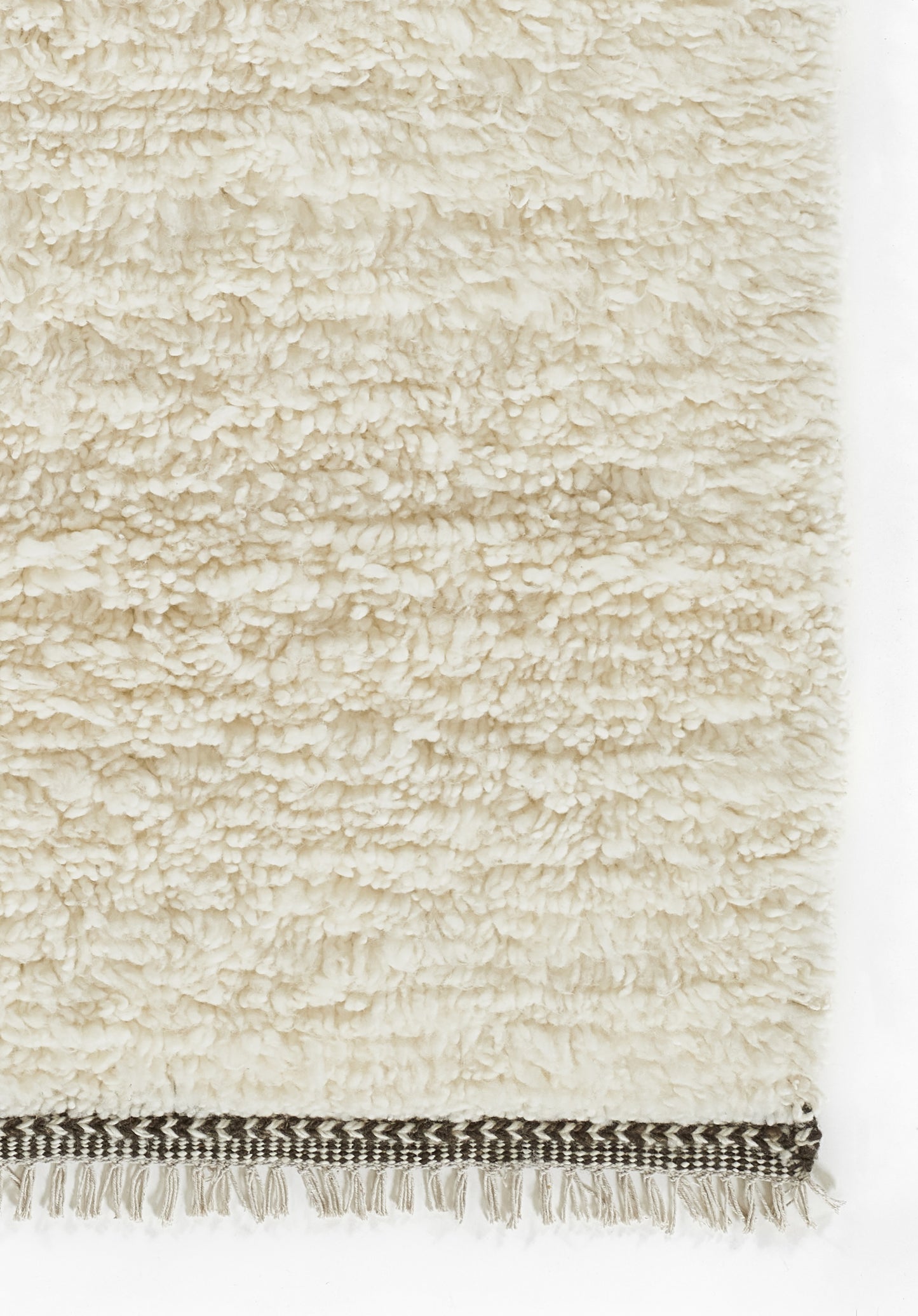 Cream shag rug with dense boucle texture and a dark striped woven border with white fringe along the bottom edge.