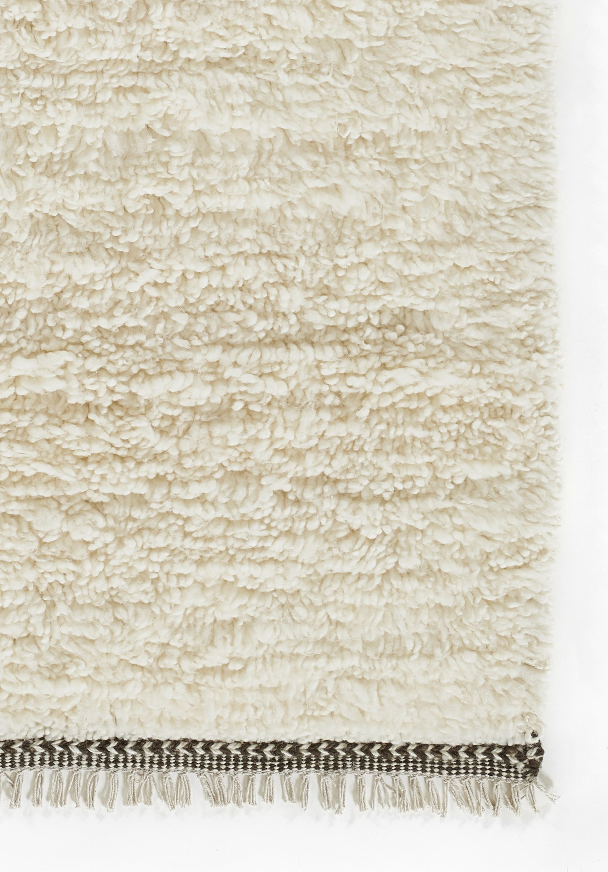 Cream shag rug with dense boucle texture and a dark striped woven border with white fringe along the bottom edge.