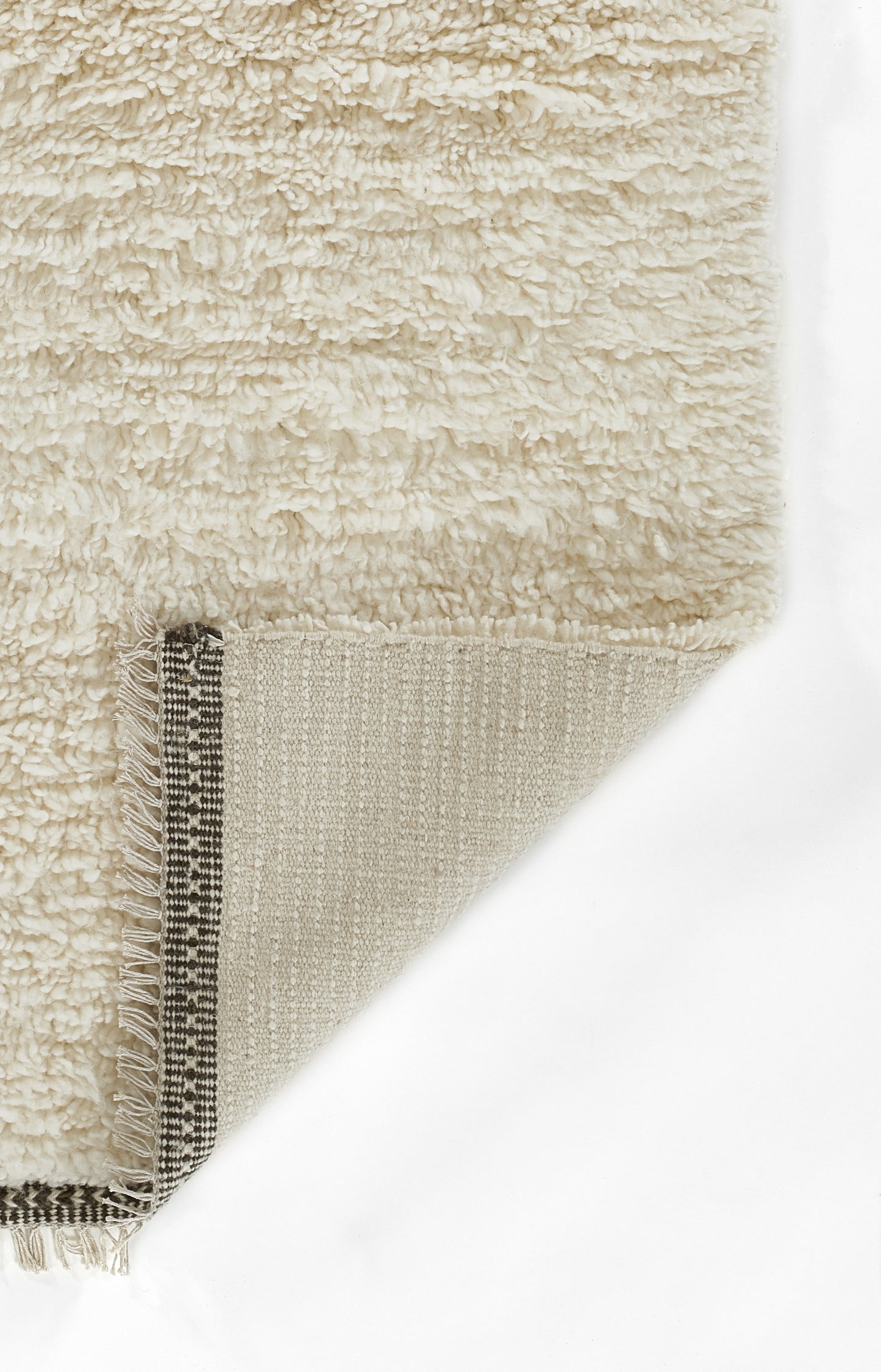 Cream shag rug with dense plush pile; folded corner reveals woven striped underside and fringe.