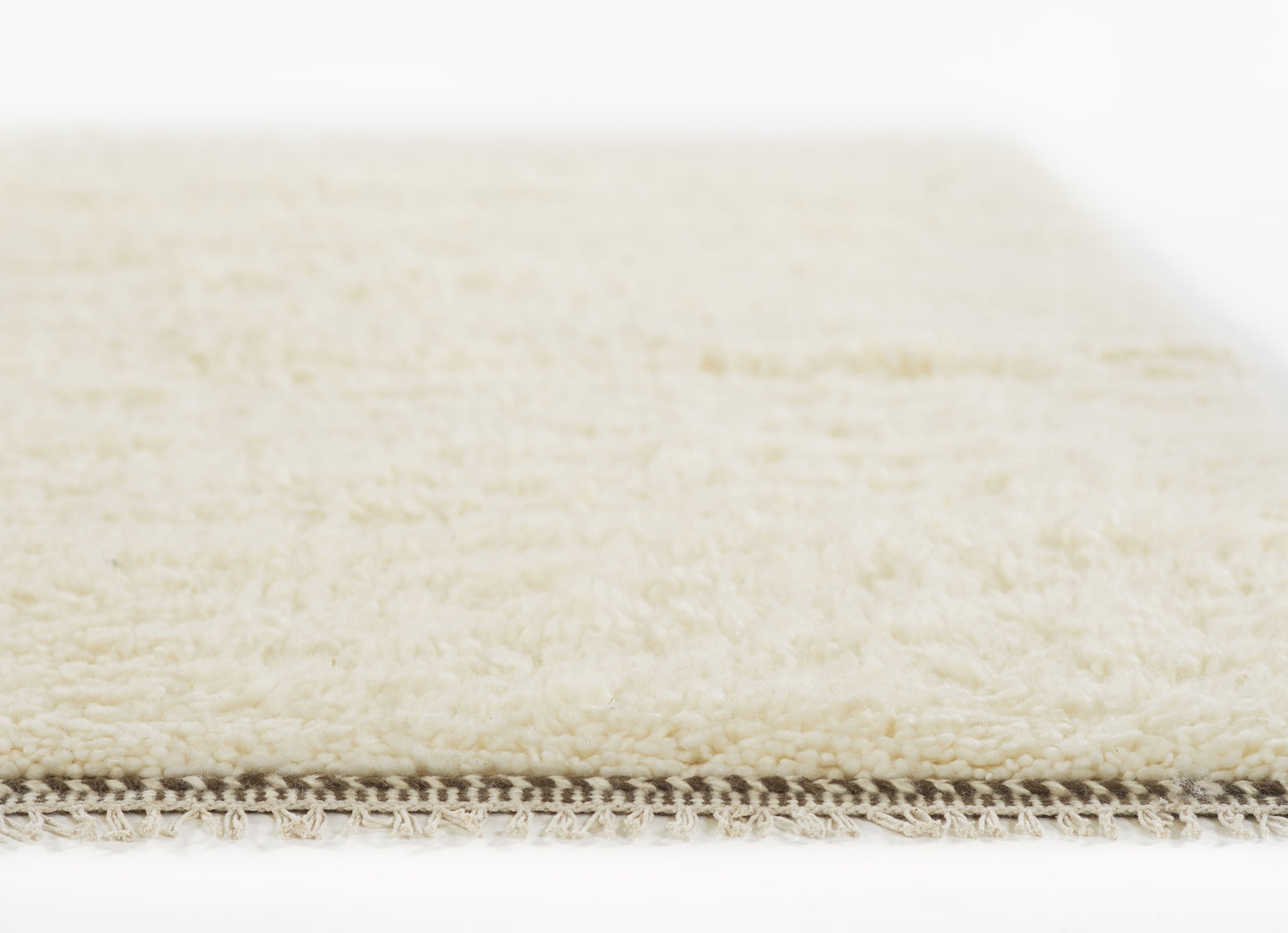 Cream shag rug close-up showing soft ivory pile and beige braided fringe along edge