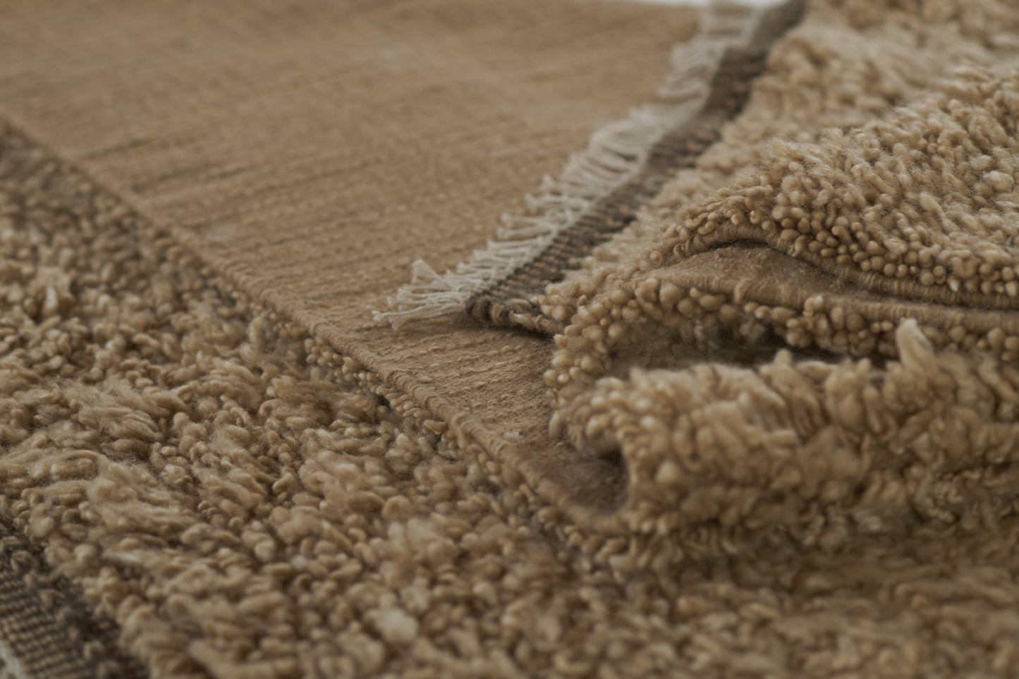 Natural beige shag rug close-up with soft fluffy pile and woven edge fringe.
