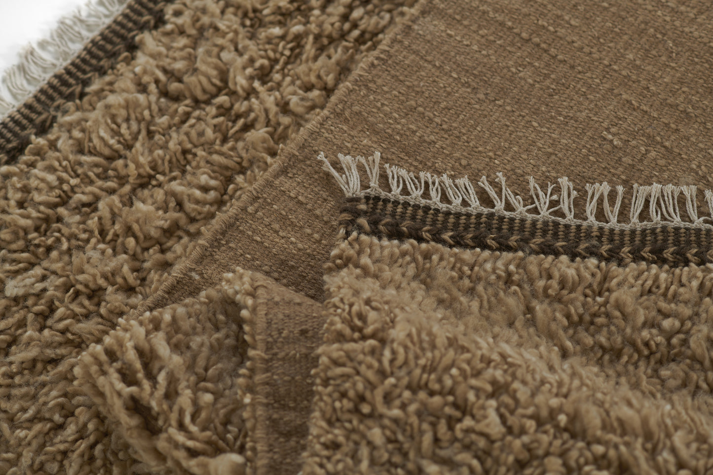 Natural brown shag rug with dense plush beige pile, fringed edge and woven border; cozy boho-style floor covering.