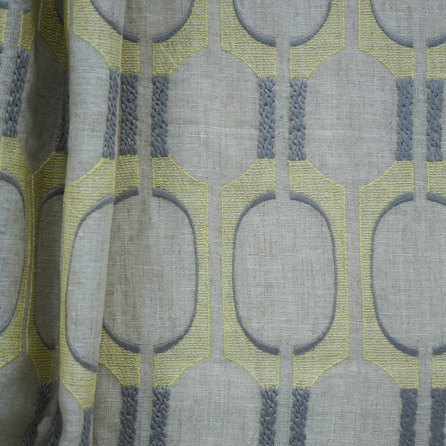 Grey linen-look fabric with lime-yellow geometric oval motifs outlined in grey; braided grey vertical accents.