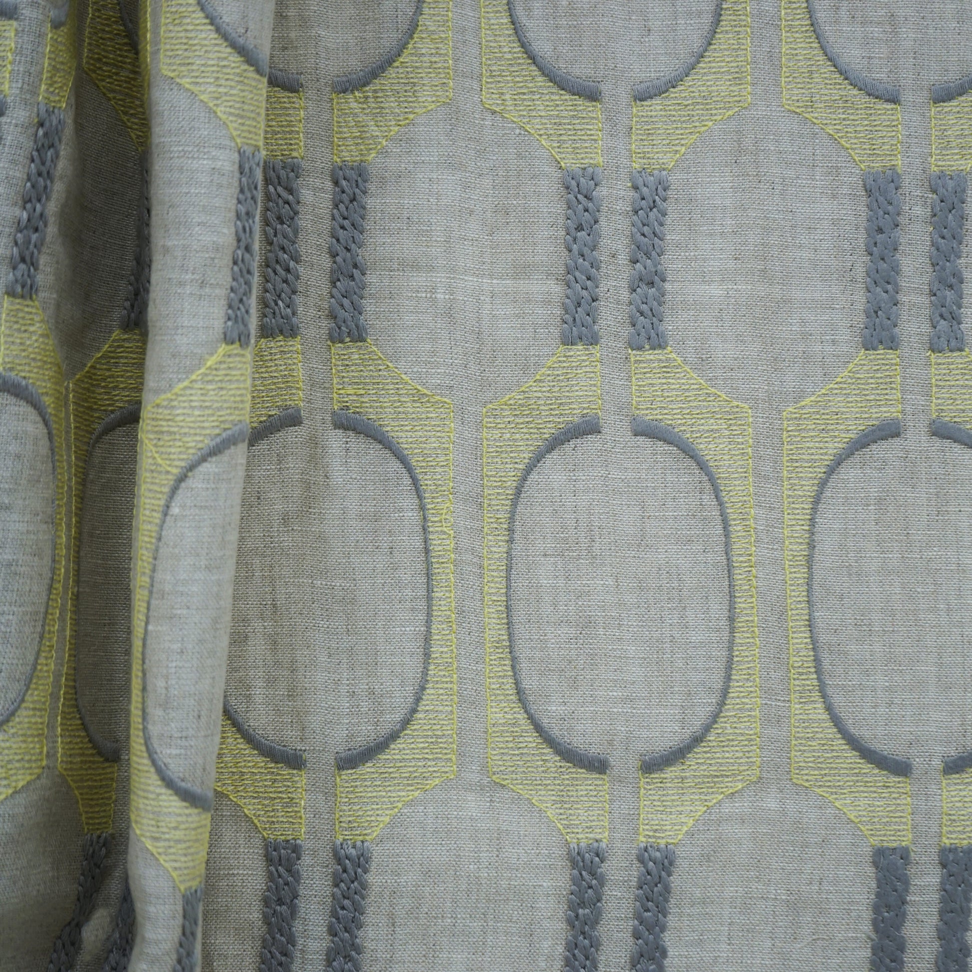 Grey linen-look fabric with lime-yellow geometric oval motifs outlined in grey; braided grey vertical accents.
