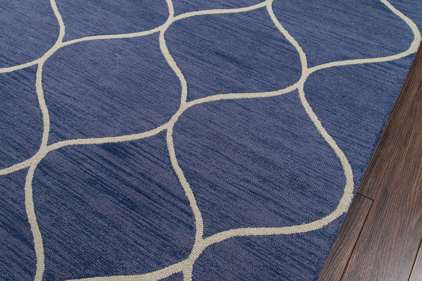 Blue rug with cream curved lattice pattern and plush texture beside dark wood flooring.