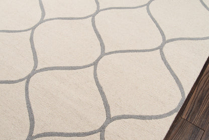 Beige area rug with gray irregular stone-grid pattern; soft woven texture, dark wood floor edge.