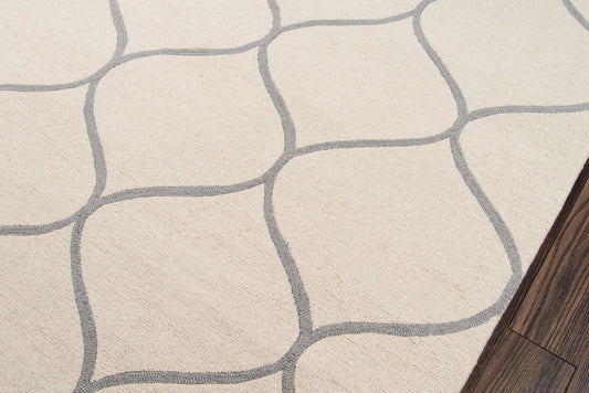 Beige area rug with gray irregular stone-grid pattern; soft woven texture, dark wood floor edge.
