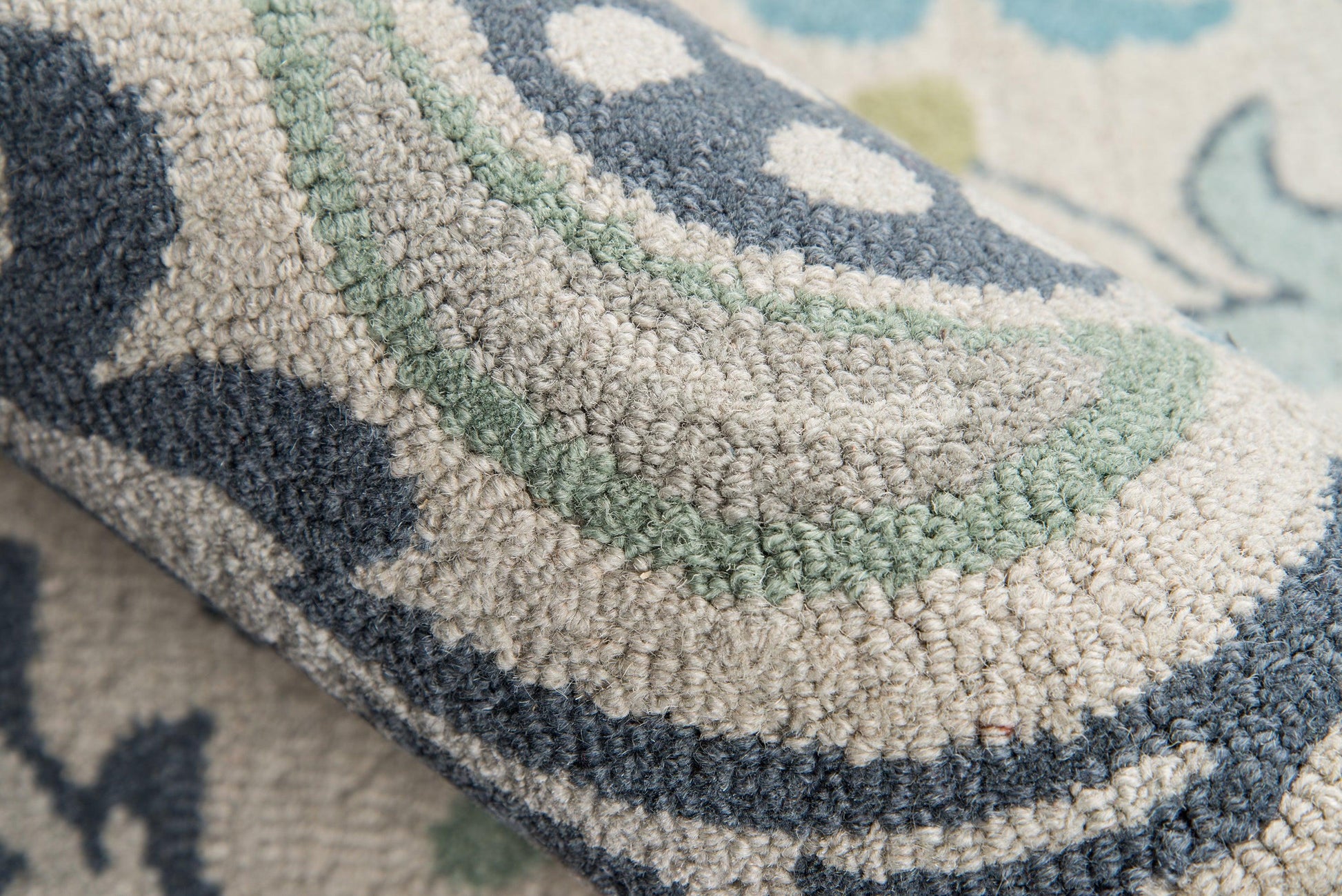 Close-up of a rolled corner on a blue, gray, beige & sage green geometric patterned rug with a textured loop pile.