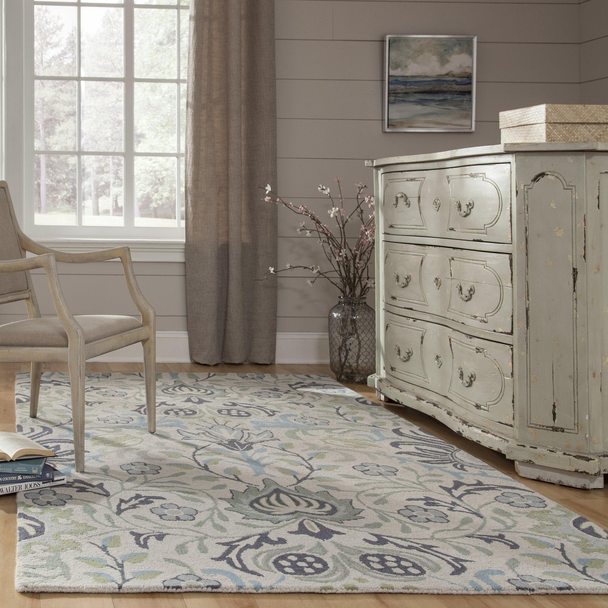 Shabby chic pale blue area rug with cream and teal floral motif beside a distressed light-blue dresser and neutral chair.