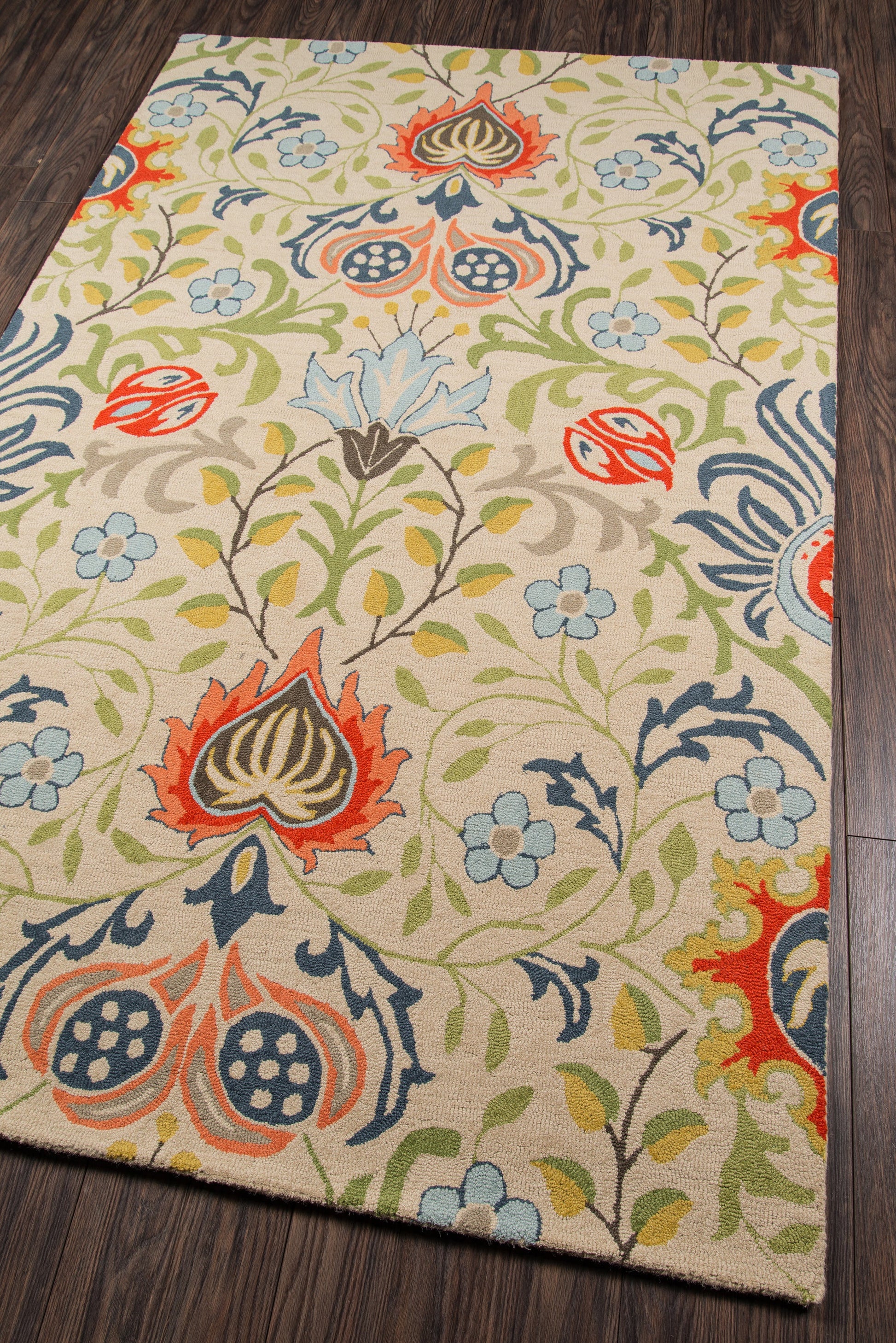 Rectangular beige area rug with a stylized botanical floral pattern in red, blue, green and orange on a dark wood floor.