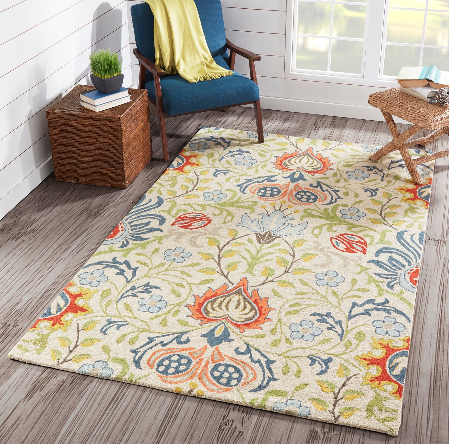 Cream floral area rug with multicolor blue, green, orange-red pattern under blue upholstered chair in bright room.