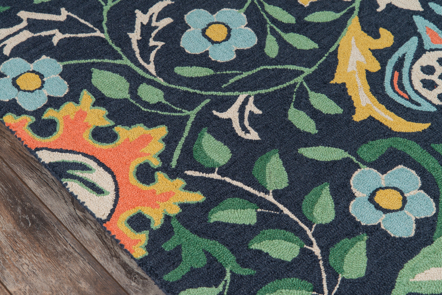 Navy floral area rug with teal flowers, green leaves and orange-yellow accents, partly on a wood floor.