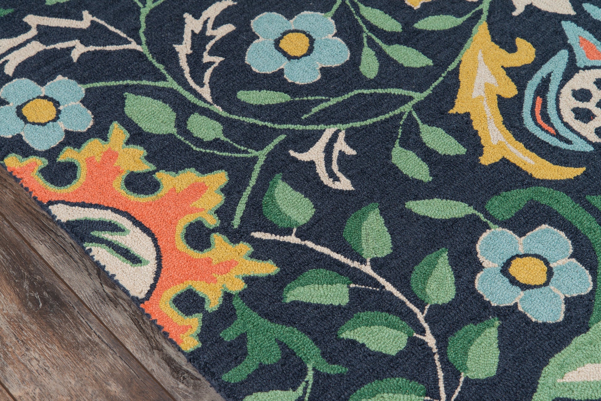 Navy floral rug with teal-blue flowers, green leaves, yellow centers; orange accents, corner on wood floor.