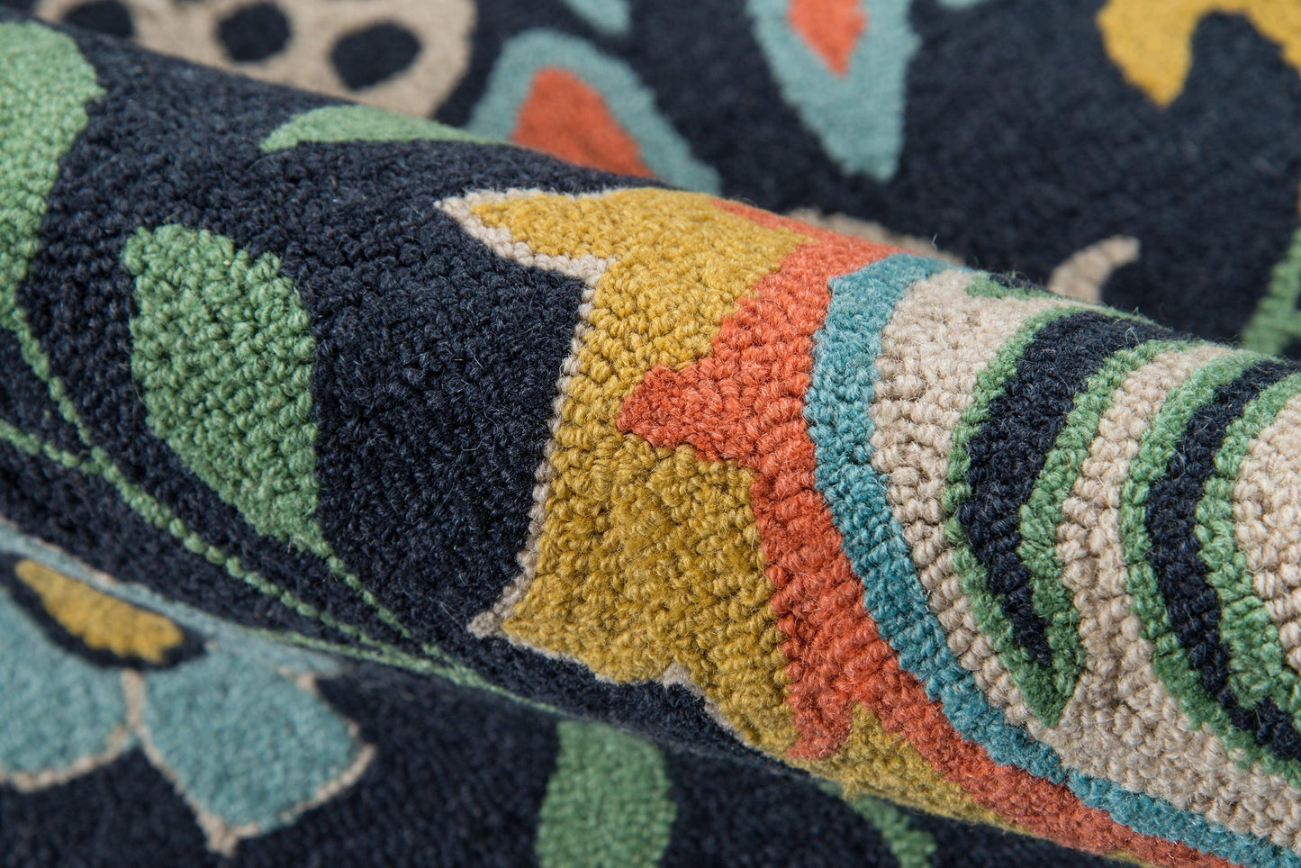 Close-up of a navy rug with a multicolor floral pattern; tufted pile in green, mustard, coral, teal, with a rolled edge.