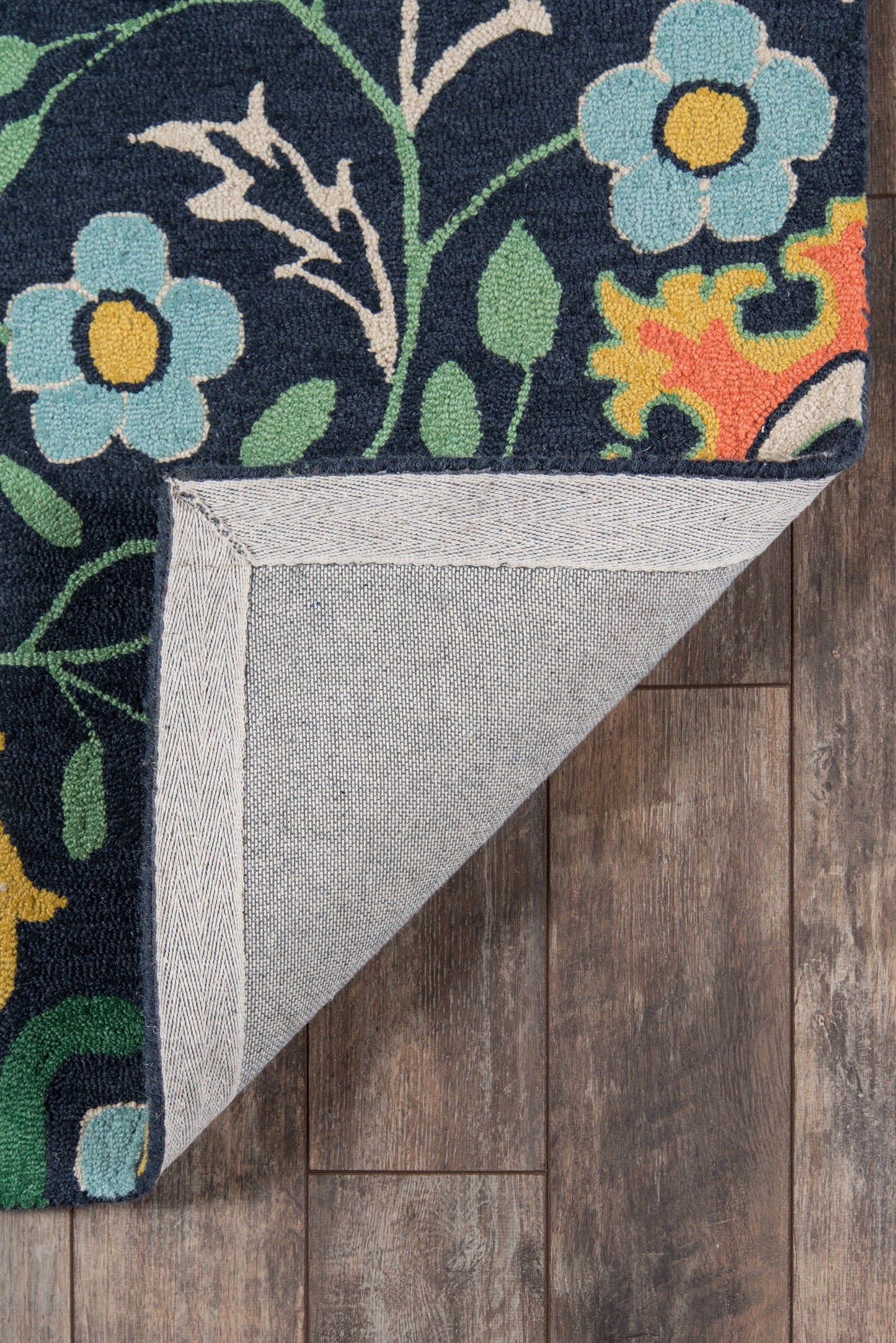 Navy floral rug with blue flowers & green leaves; folded corner shows light gray backing on wood floor.