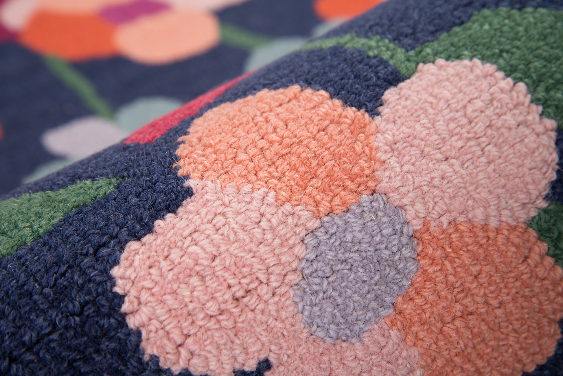 Close-up of a soft tufted rug with navy base, peach/pink floral shapes, purple accents, and green stems.