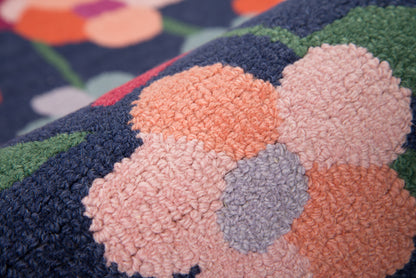 Close-up of a plush tufted rug with navy base and peach, pink, lavender blossom shapes.