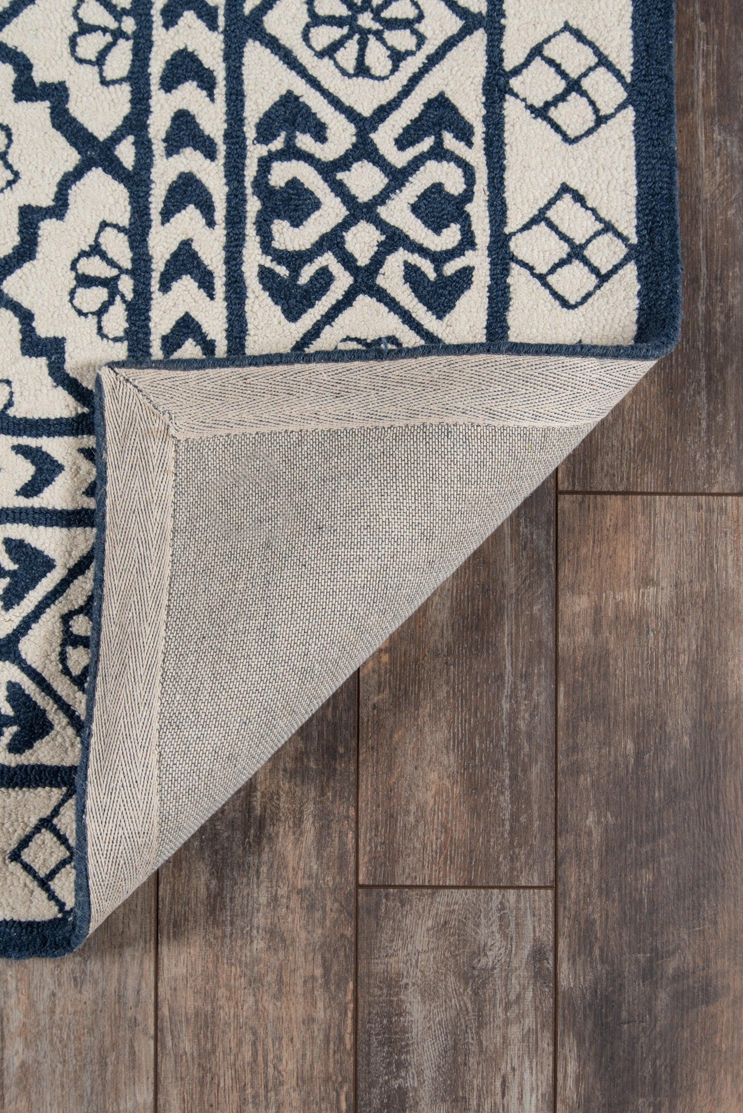 Navy blue and ivory rug with geometric floral pattern, rolled corner reveals beige underside on dark wood floor.