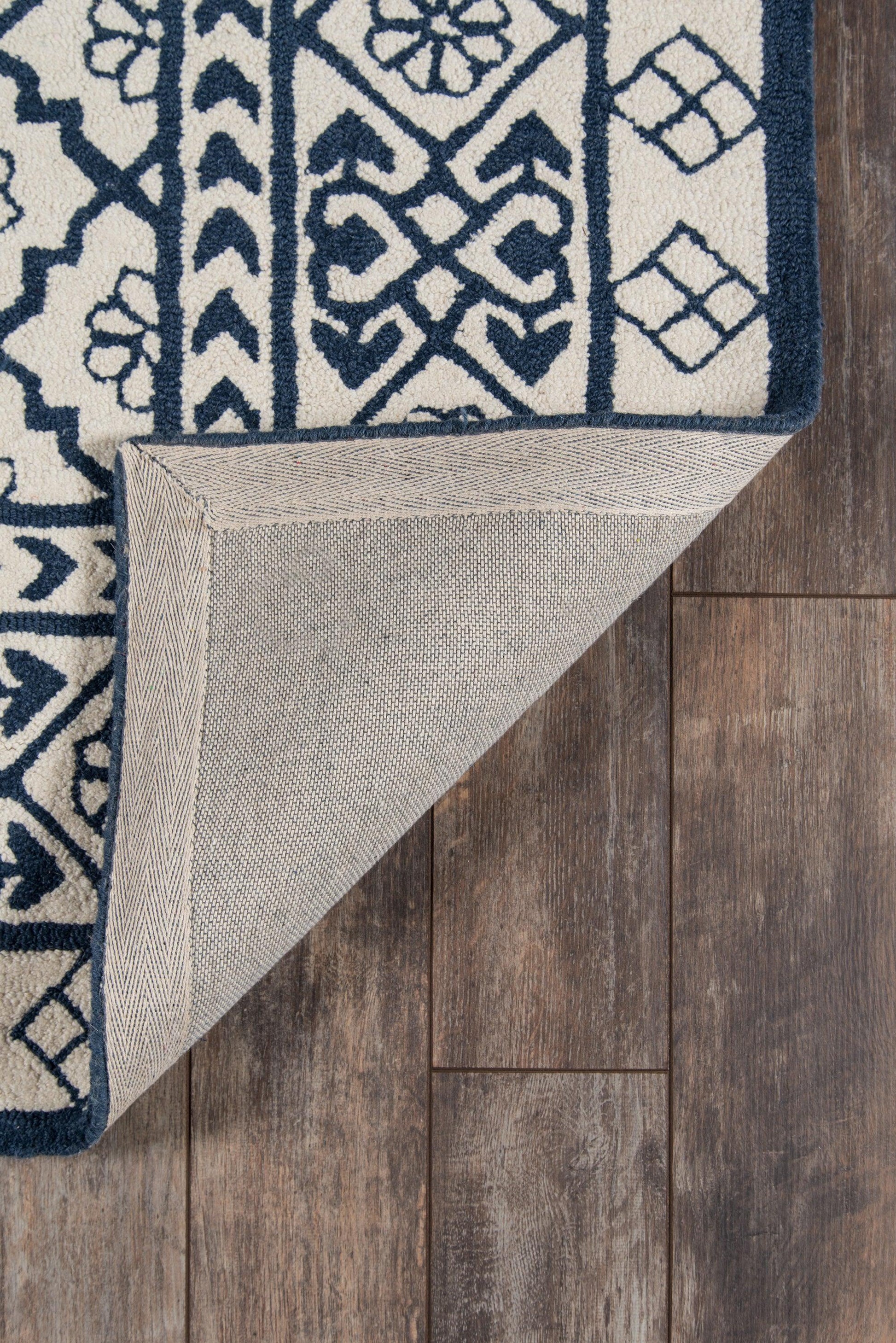 Navy blue & ivory geometric floral runner rug with ornate border, folded corner showing beige backing on wood floor.