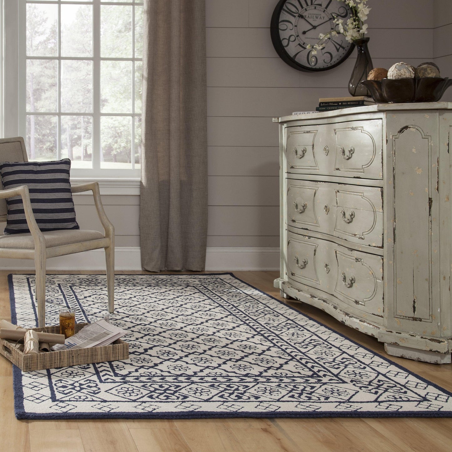 Vintage distressed pale blue dresser in a sunlit living room with a blue and ivory geometric rug, striped chair cushion, and large clock.