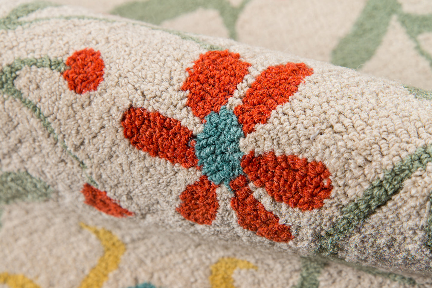 Beige textured rug close-up, red-orange flower with teal center and green border.