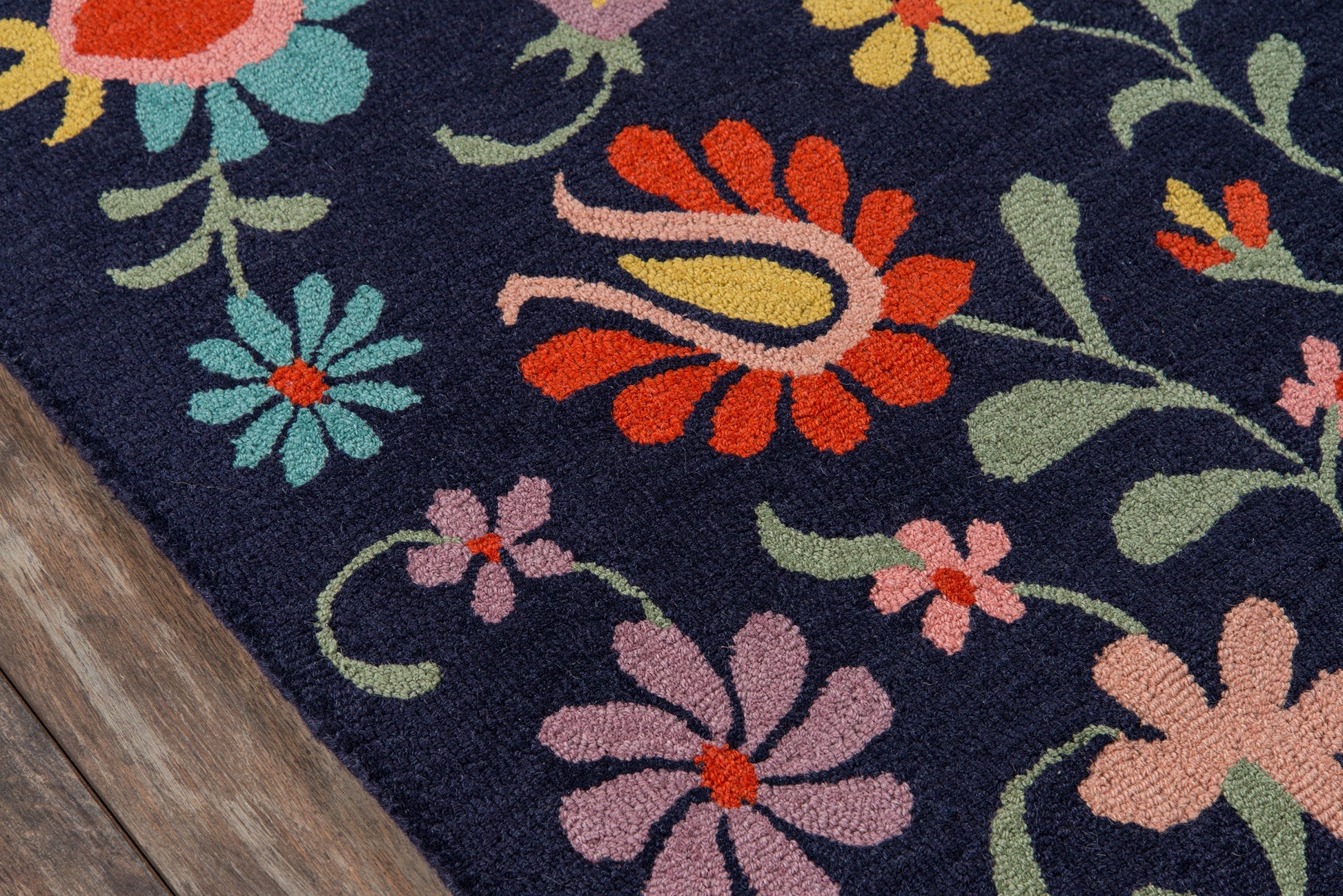 Navy rug with vibrant floral pattern in pink, orange, teal, lilac and green; soft textured pile on a wooden floor edge.