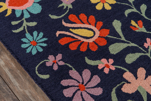 Navy blue rug with bright multicolor floral pattern in orange, pink, teal, & lime green on a wood floor.