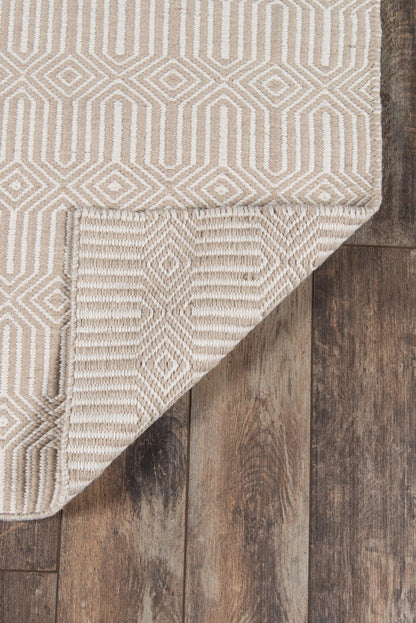 Beige geometric woven rug with diamond pattern and ivory lines, rolled corner on dark wood floor.