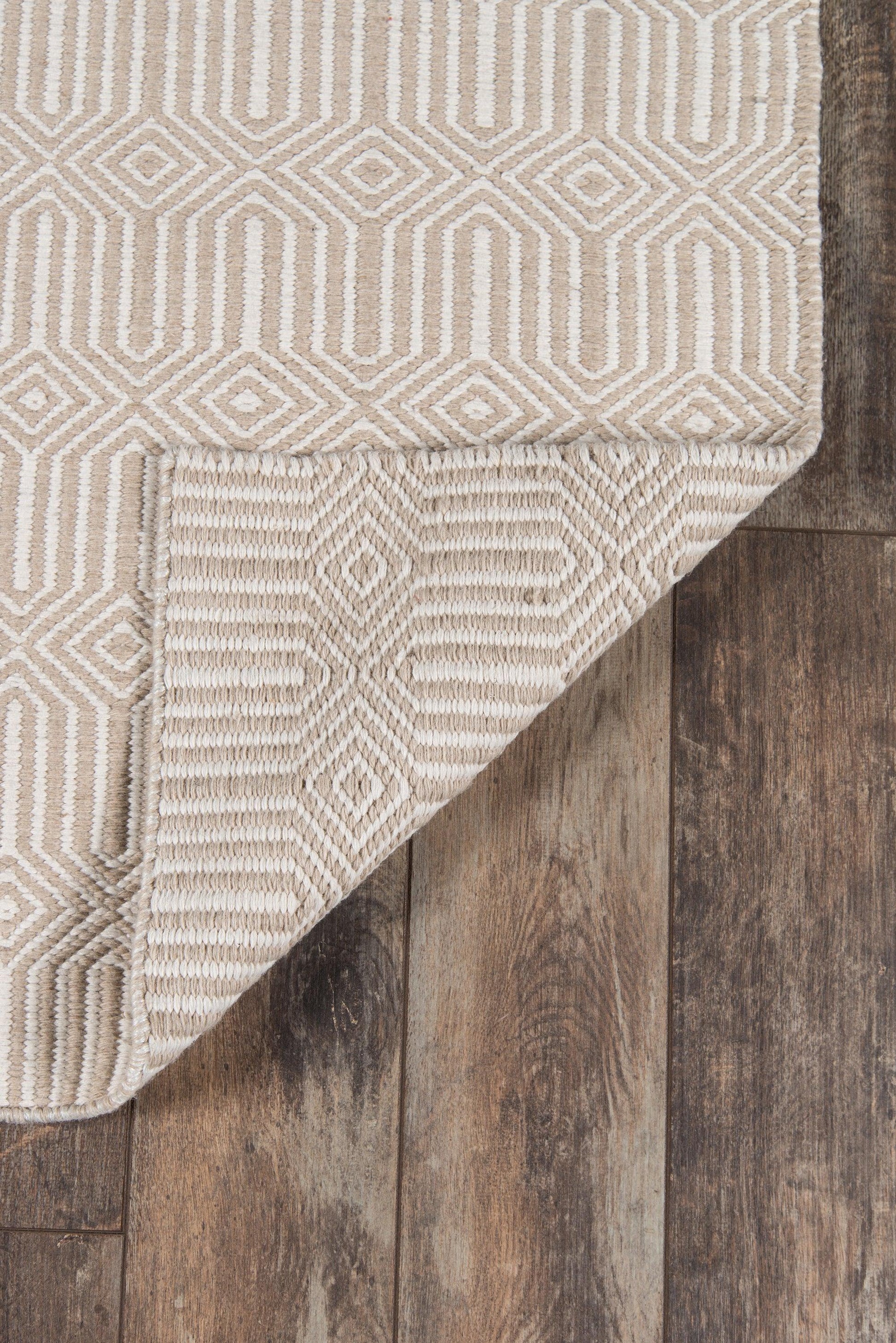 Beige rug with white geometric diamond pattern; folded corner on dark wood plank floor.