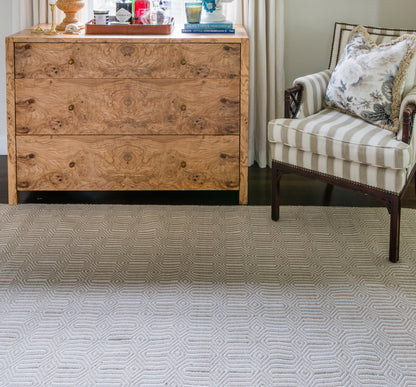 Natural burl wood dresser with four drawers and brass knobs, beside striped beige armchair with floral cushion on a geometric rug.