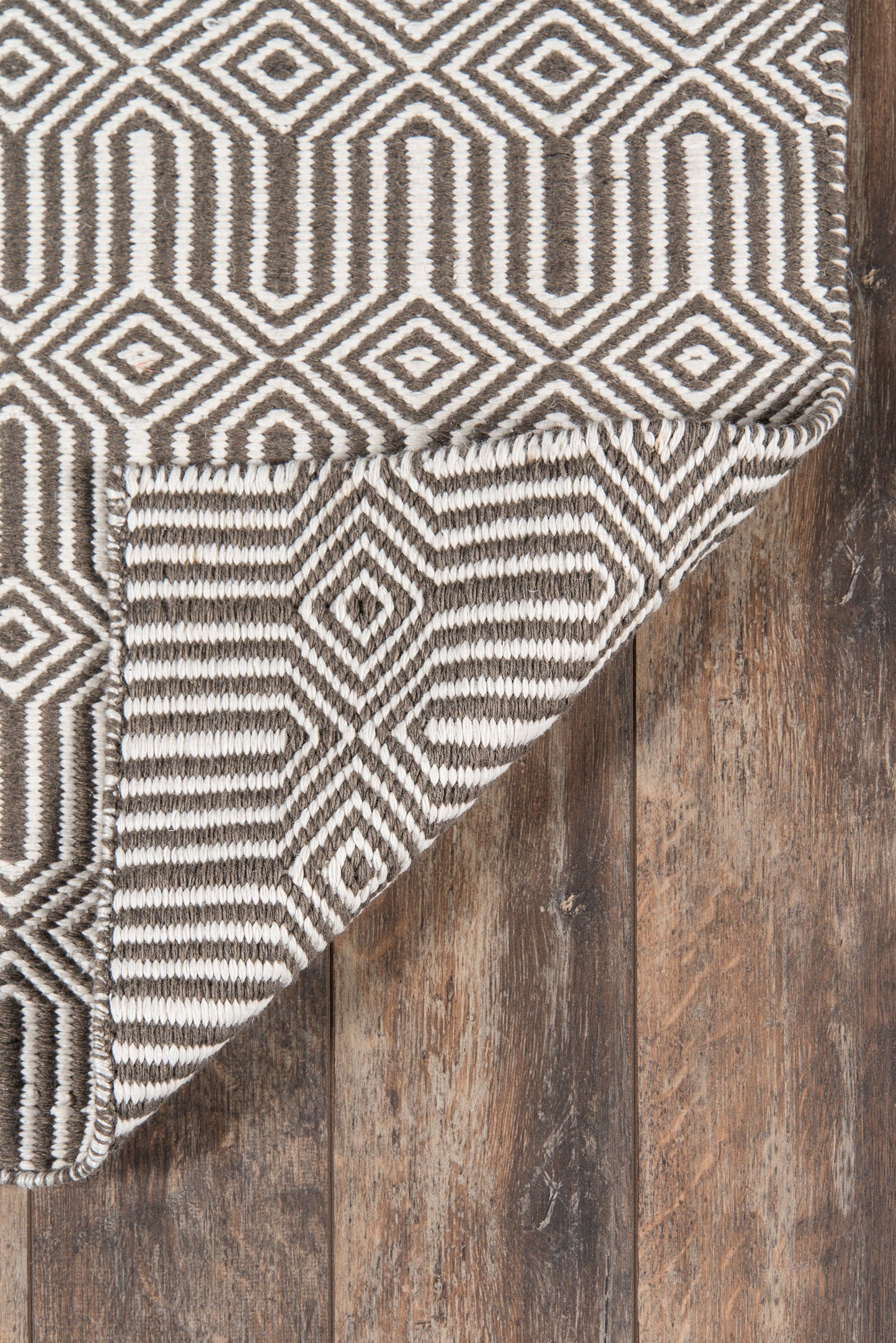 Brown and ivory geometric rug with diamond motif, folded corner over rustic wooden floor.