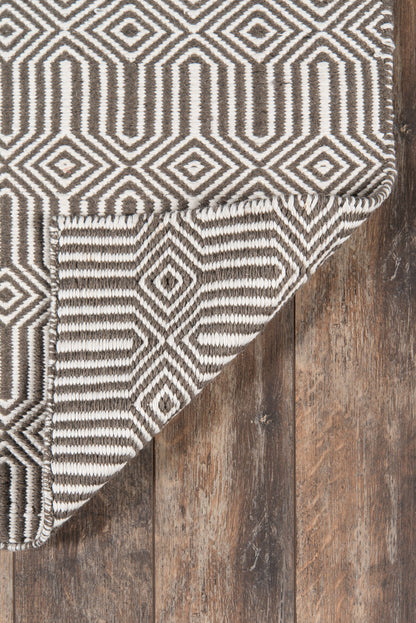 Geometric brown and ivory rug with diamond and stepped-line patterns, woven texture, folded corner on rustic wood floor.