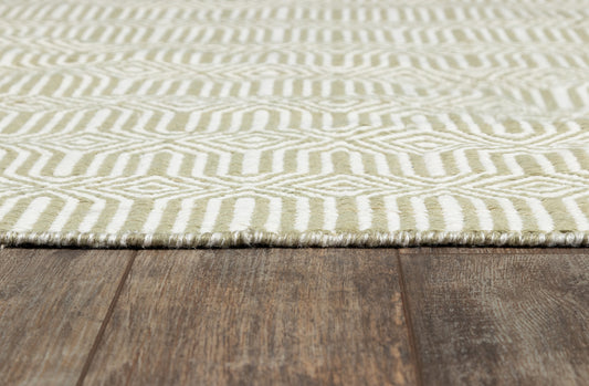 Olive-green and ivory geometric rug with diamond/chevron motif and fringed edge on wood floor.