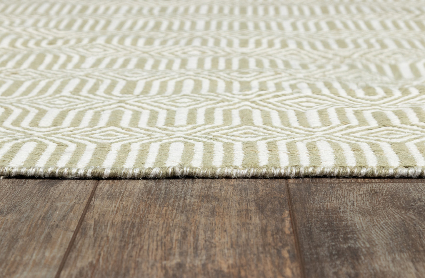 Cream and sage geometric patterned rug with fringe edge on dark wooden floor.