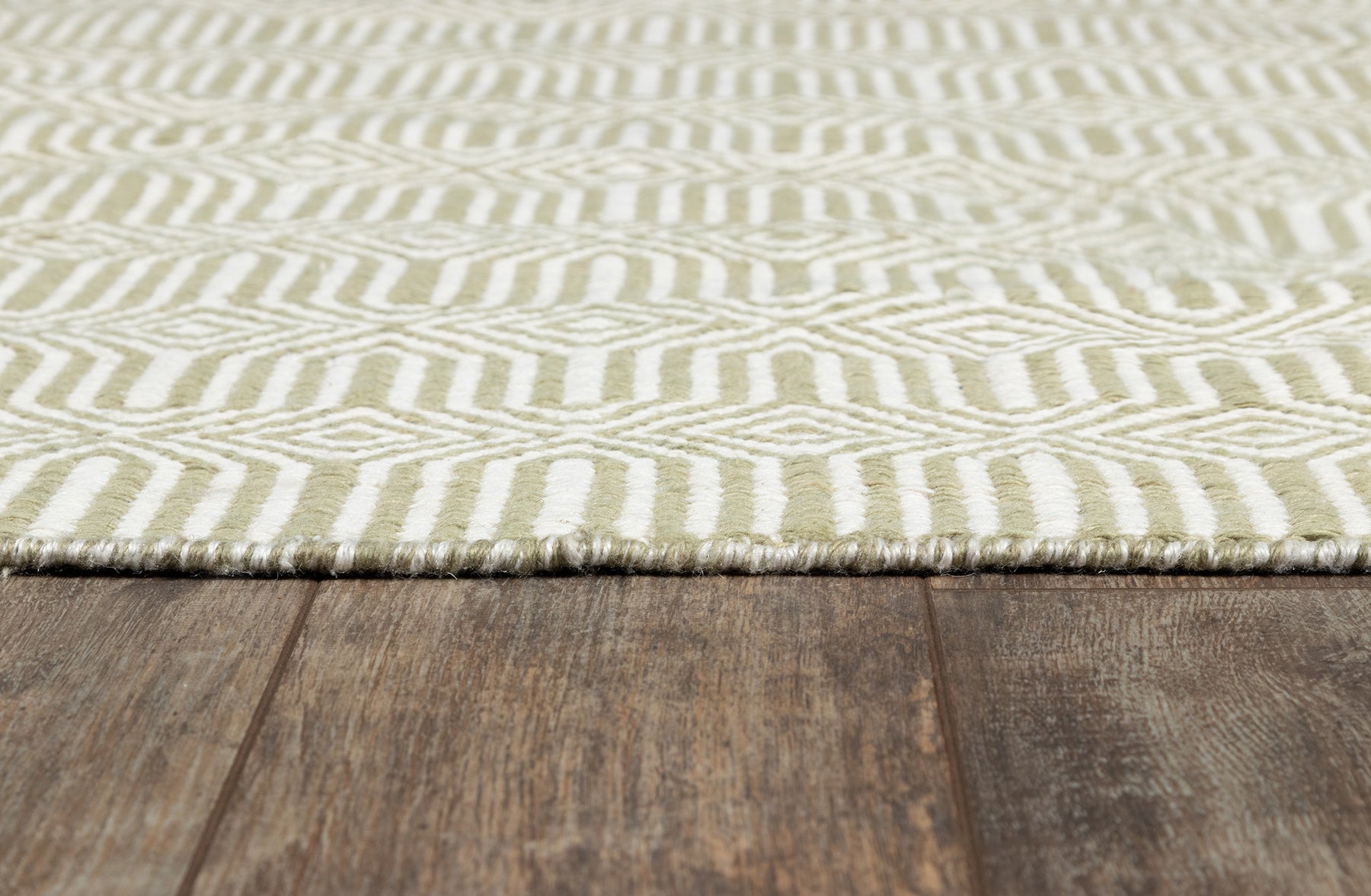 Cream and sage geometric patterned rug with fringe edge on dark wooden floor.