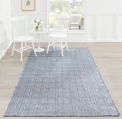 Navy and white diamond-pattern rug runner on light wood floor beside white chairs and round table.