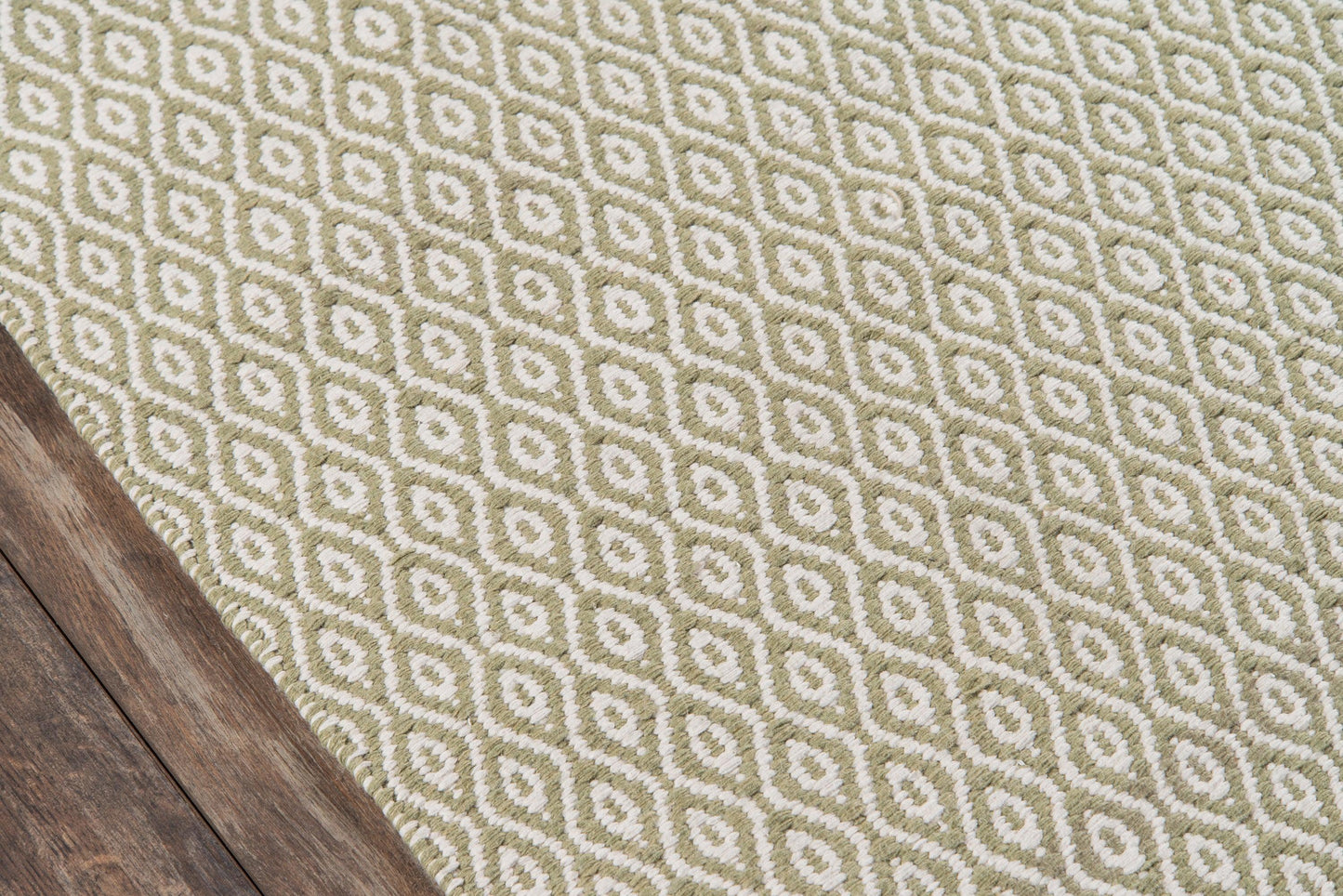 Olive-green and cream geometric diamond rug on dark wood floor with woven texture; modern contemporary style.
