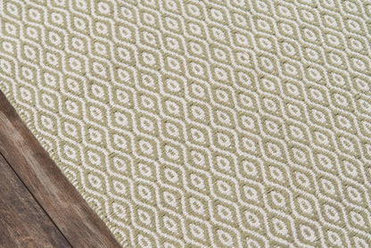Olive-green and cream geometric diamond rug on dark wood floor with woven texture; modern contemporary style.