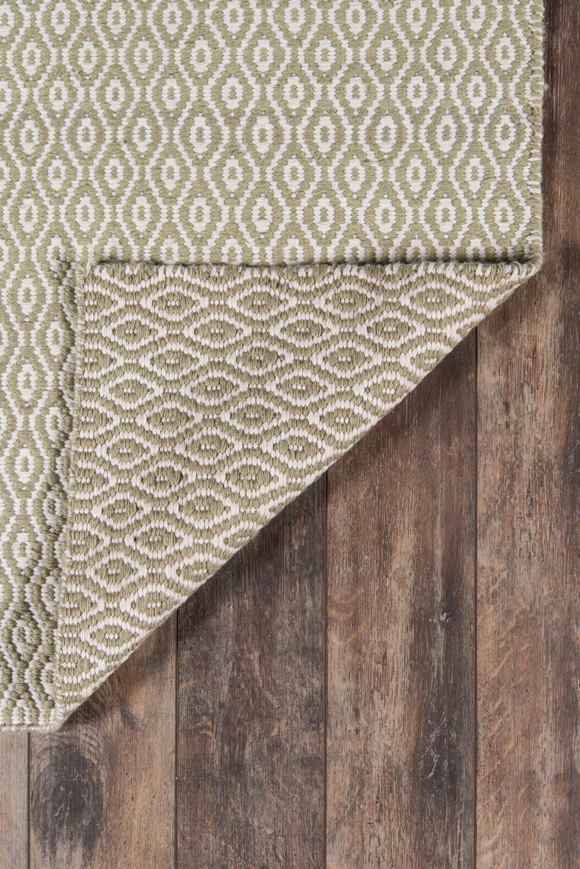 Olive green & cream geometric woven rug with oval motif, textured surface, folded corner shows underside, on wood floor.