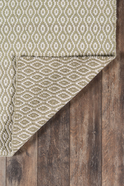 Olive green & cream geometric woven rug with oval motif, textured surface, folded corner shows underside, on wood floor.