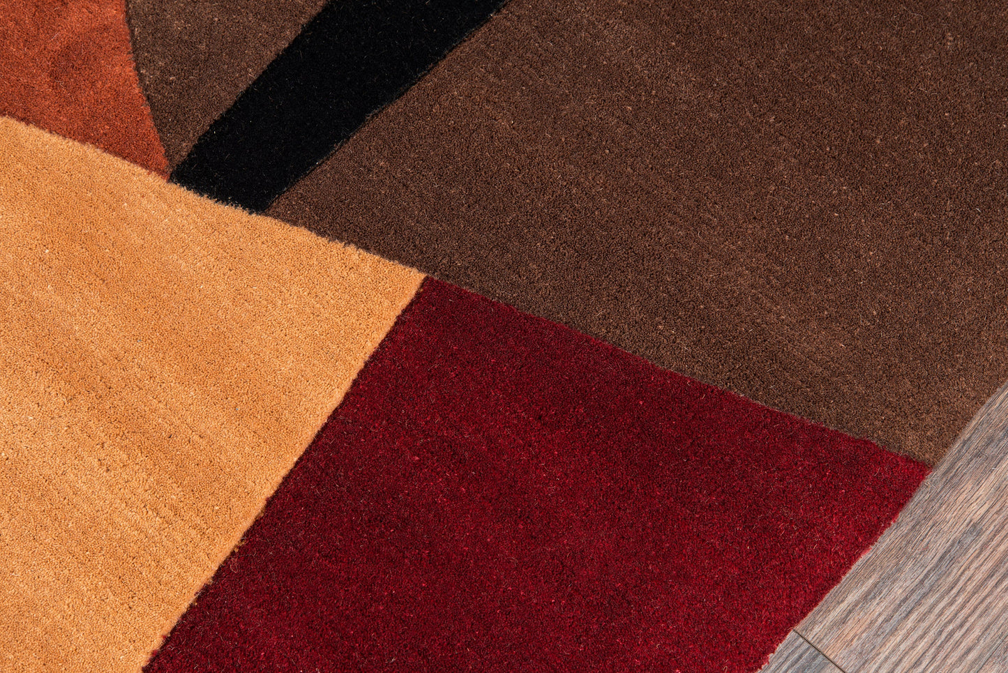 Geometric patchwork runner on a wood floor in orange, tan, red, brown and black, size 2'6" x 8'.