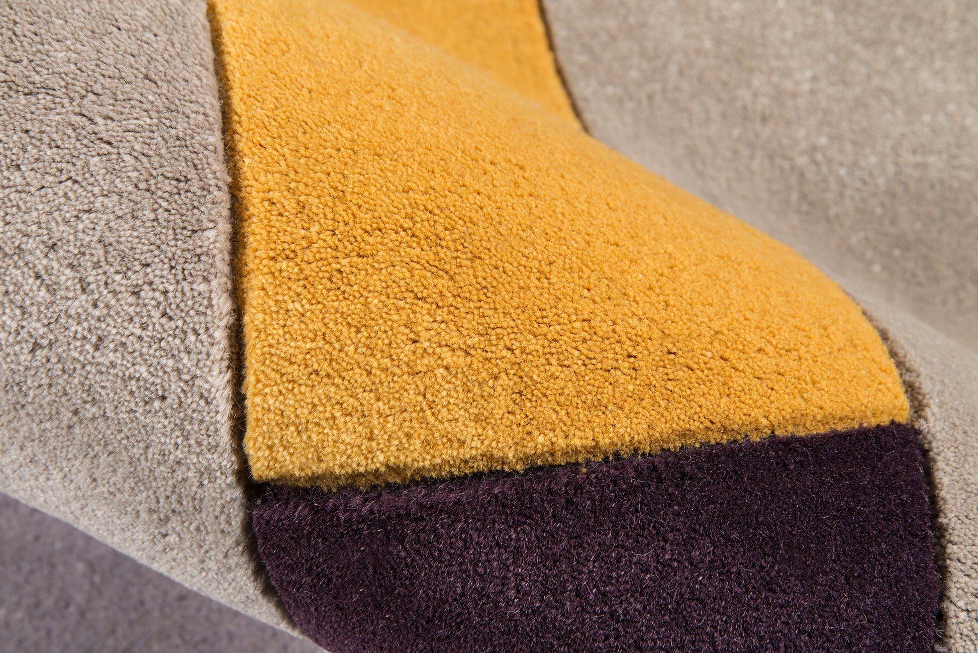 Close-up of plush boucle throw with color-block panels in gray, mustard yellow, and deep plum.