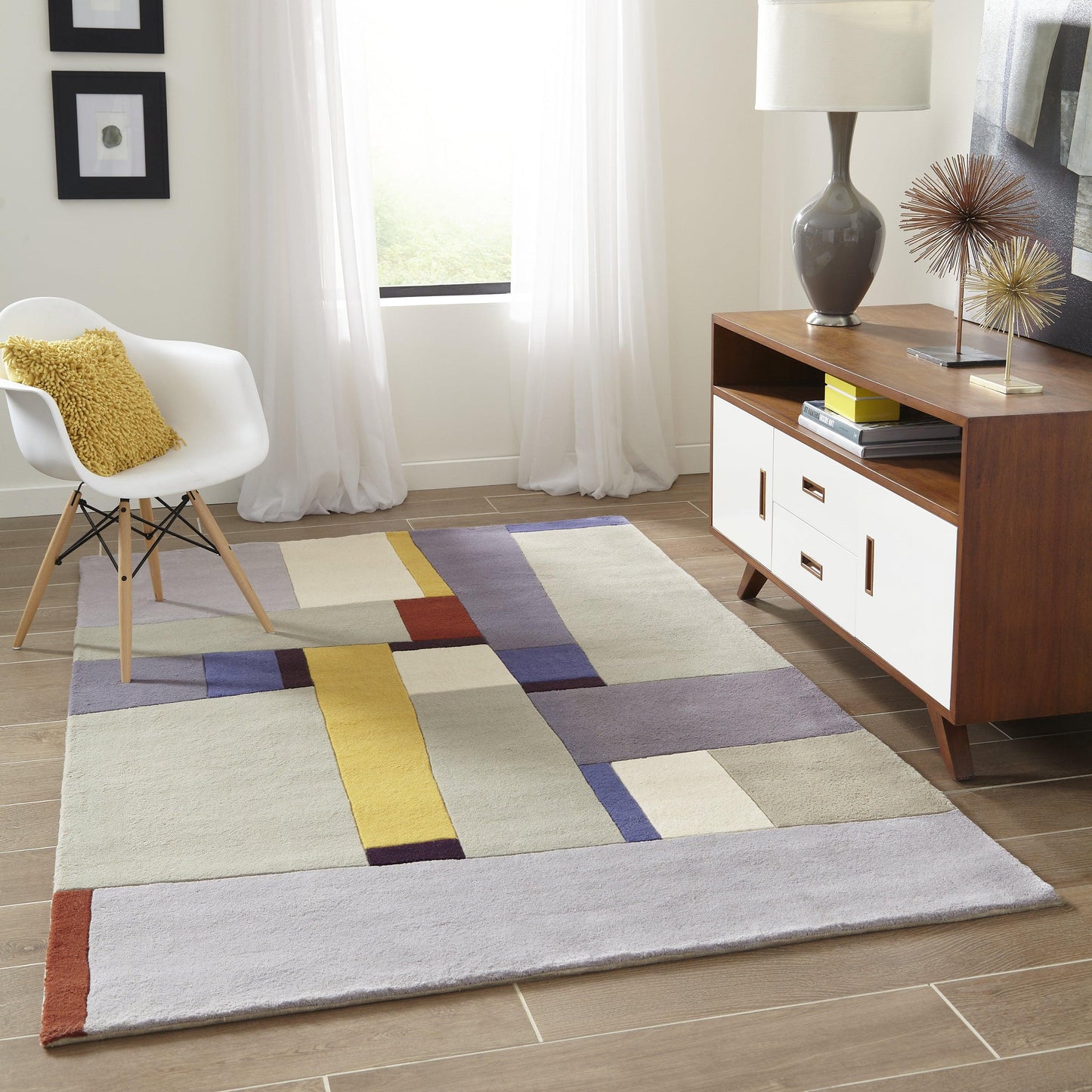 Geometric area rug in cream, gray, lavender, yellow and rust blocks on a wood floor in a modern living room.
