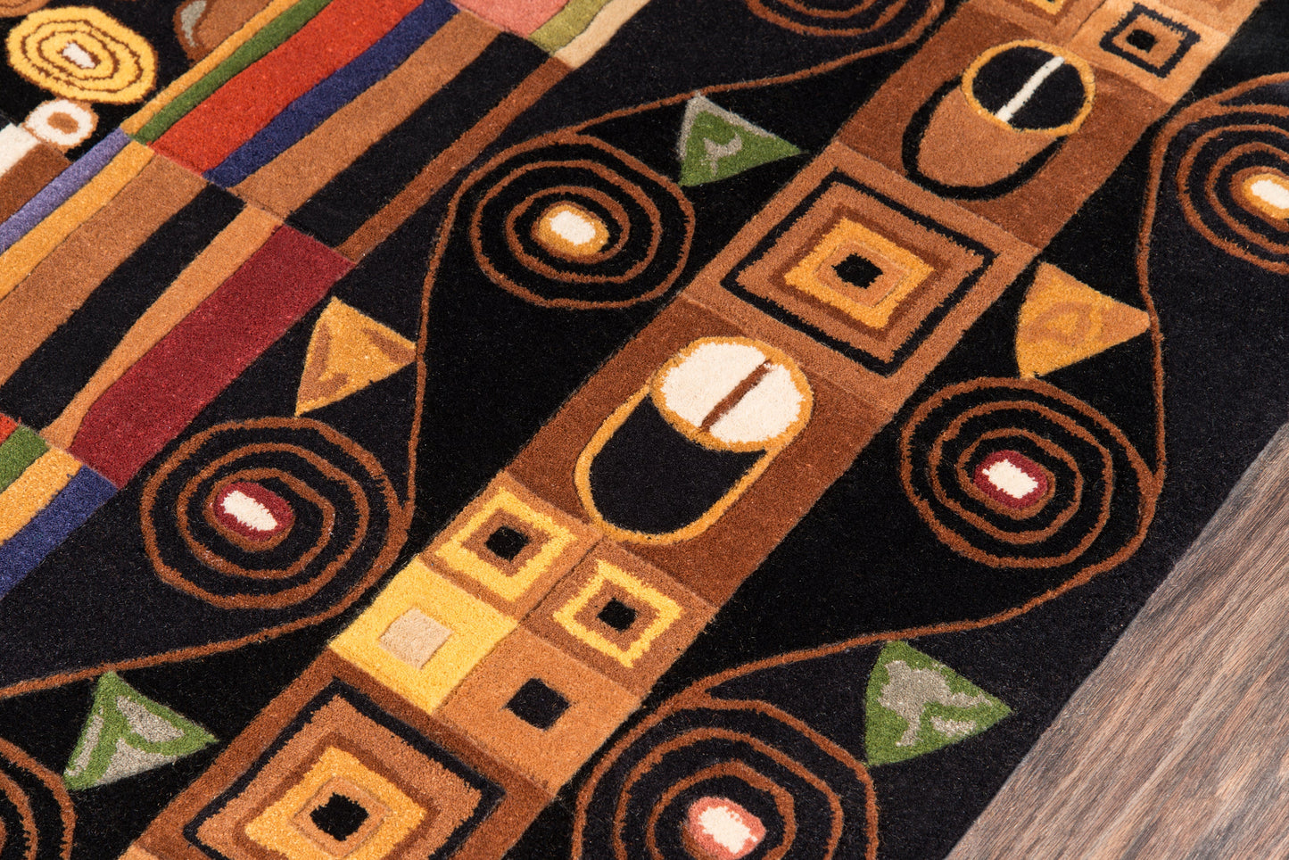 Abstract geometric area rug with black background, brown/orange squares, spirals and triangles; warm multicolor border.