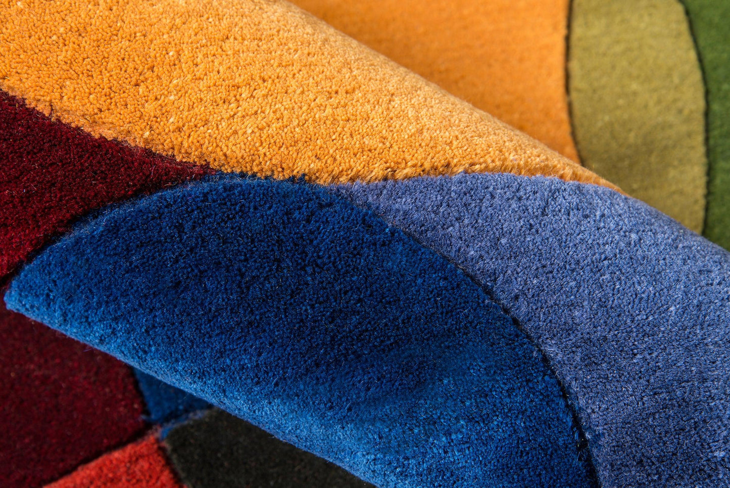 Close-up of a shaggy multicolor rug with curved color blocks in orange, blue, burgundy and olive green.
