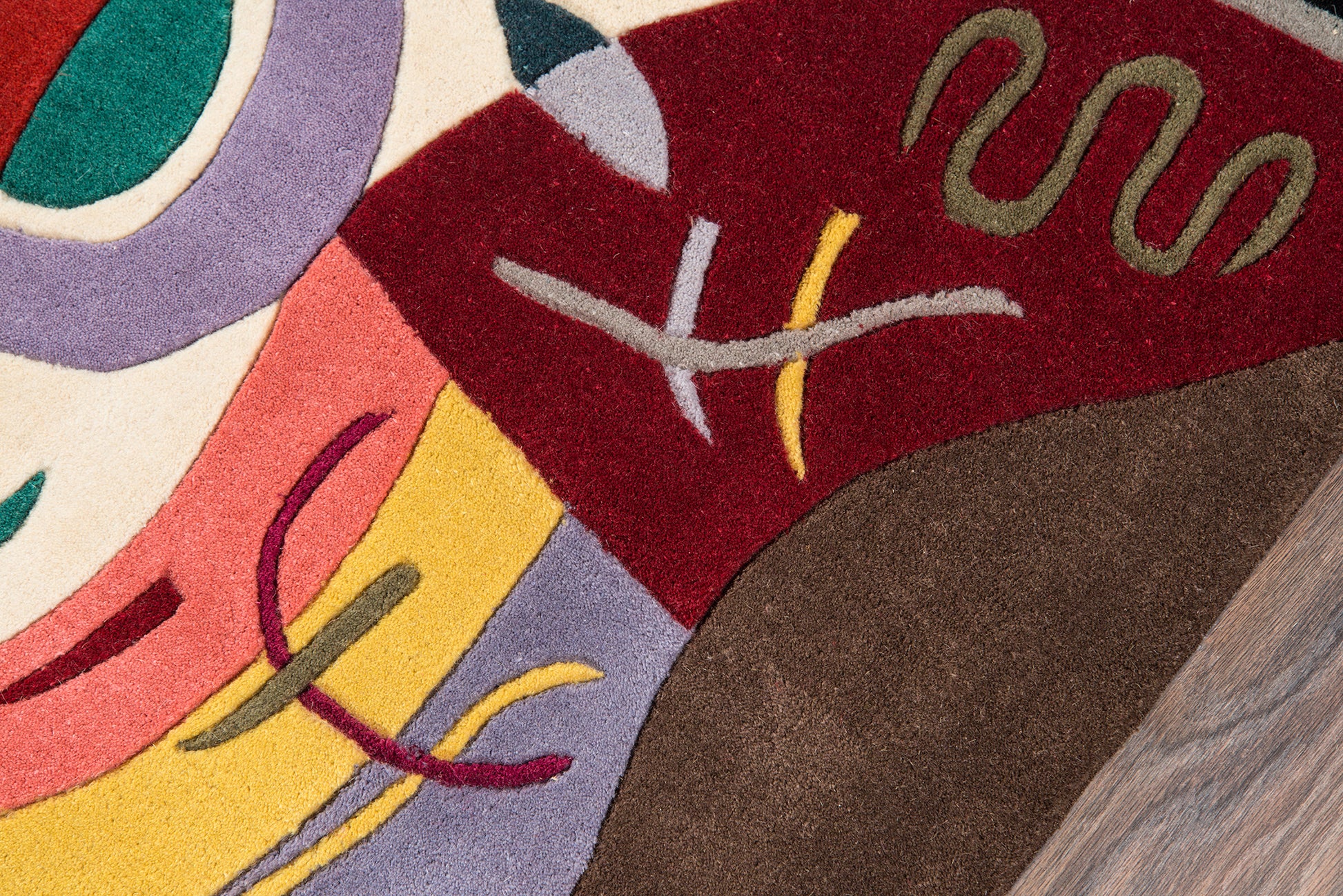 Abstract multicolor area rug with bold geometric shapes in maroon, yellow, lavender, pink, teal and brown.