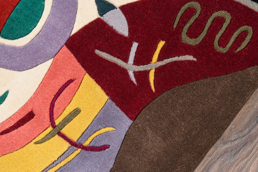 Abstract multicolor rug close-up with curved shapes in red, yellow, purple, pink, green on beige and brown, plush pile.